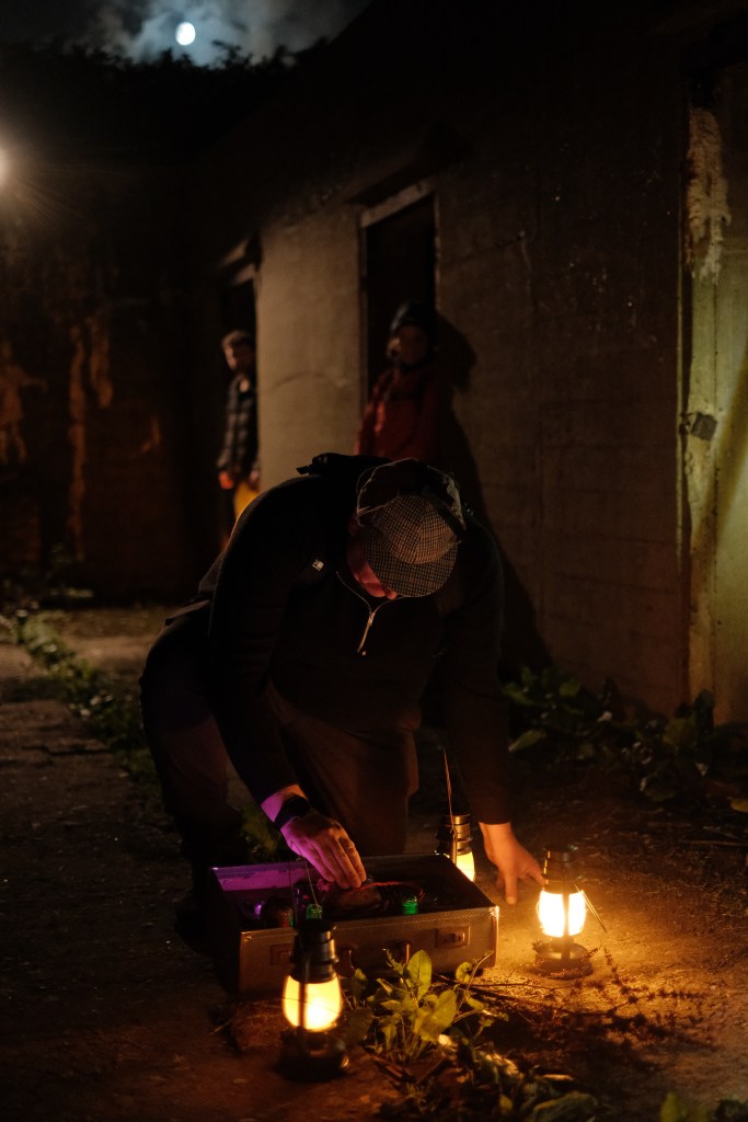 A man attempting to use a device. It is dark and he is surrounded by lanterns.