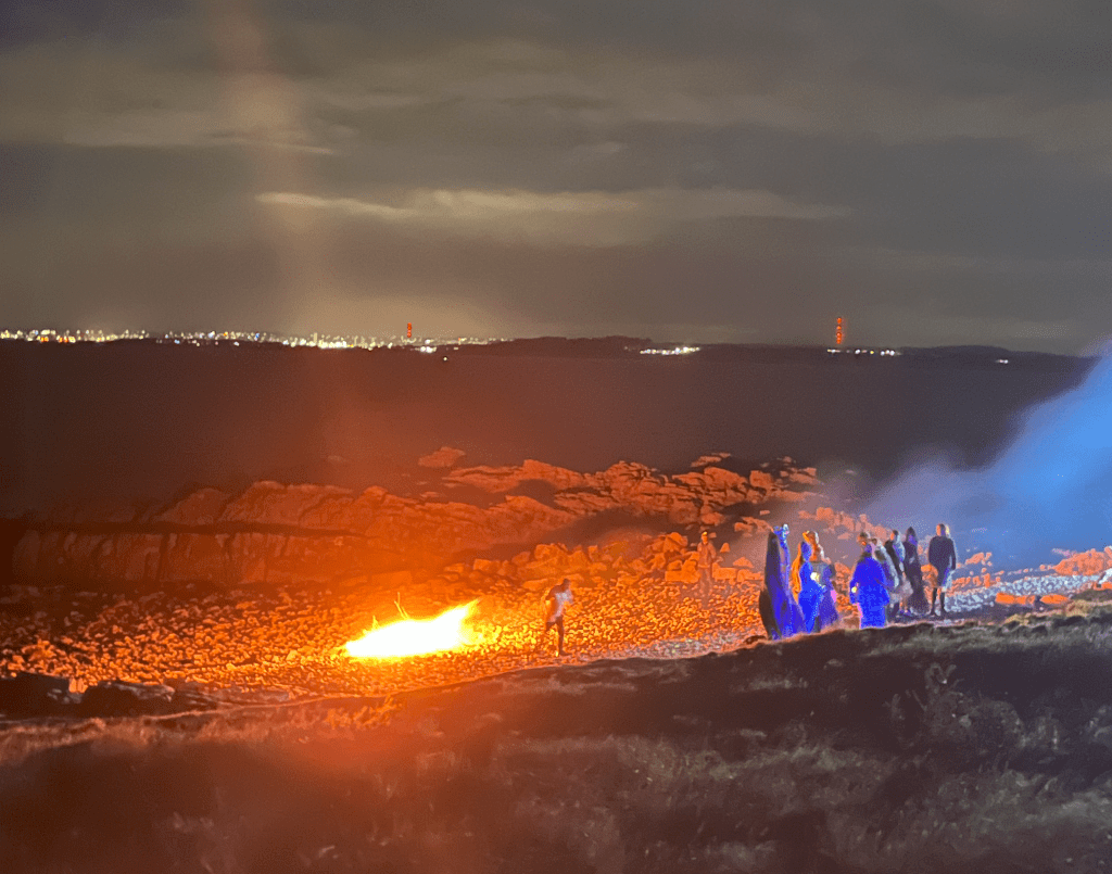 a fire on a rocky beach with beasts lined up in front of it. Three recruits remain whilst the other recruits have left.